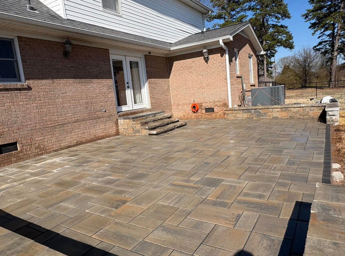 Large multi-tone paver patio with block steps to French doors and a low seating wall behind a brick home in Mooresville, NC