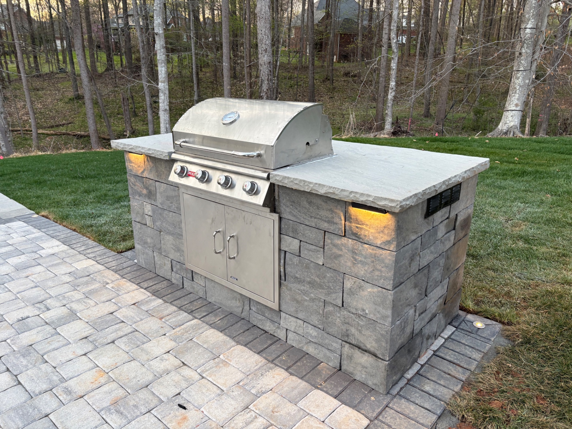 Stone veneer built-in grill island with a natural stone countertop and under-cap lighting on a paver patio in Mooresville, NC