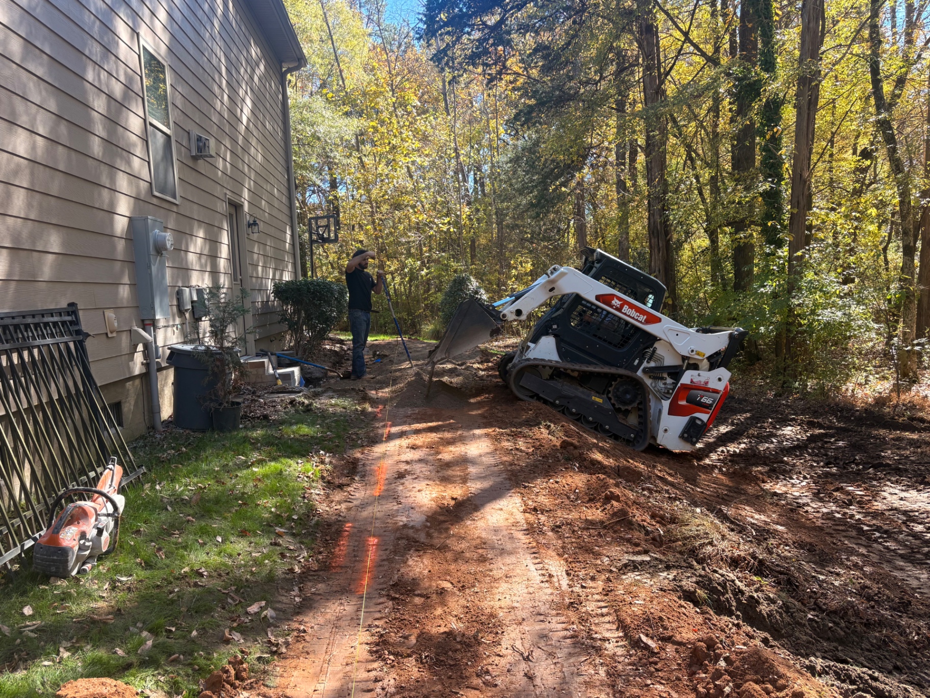 Skid steer excavating a marked drainage trench line beside a house in Mooresville, NC