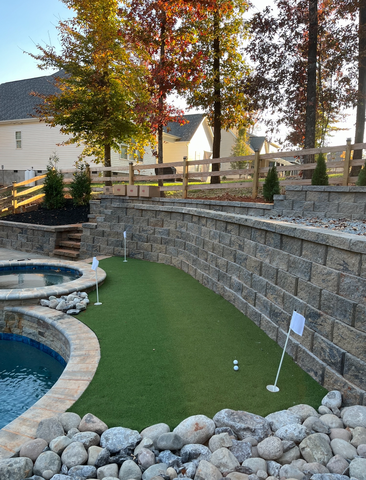 Tiered segmental block retaining walls above an artificial turf putting green beside a pool with a river rock border in Sherrills Ford, NC