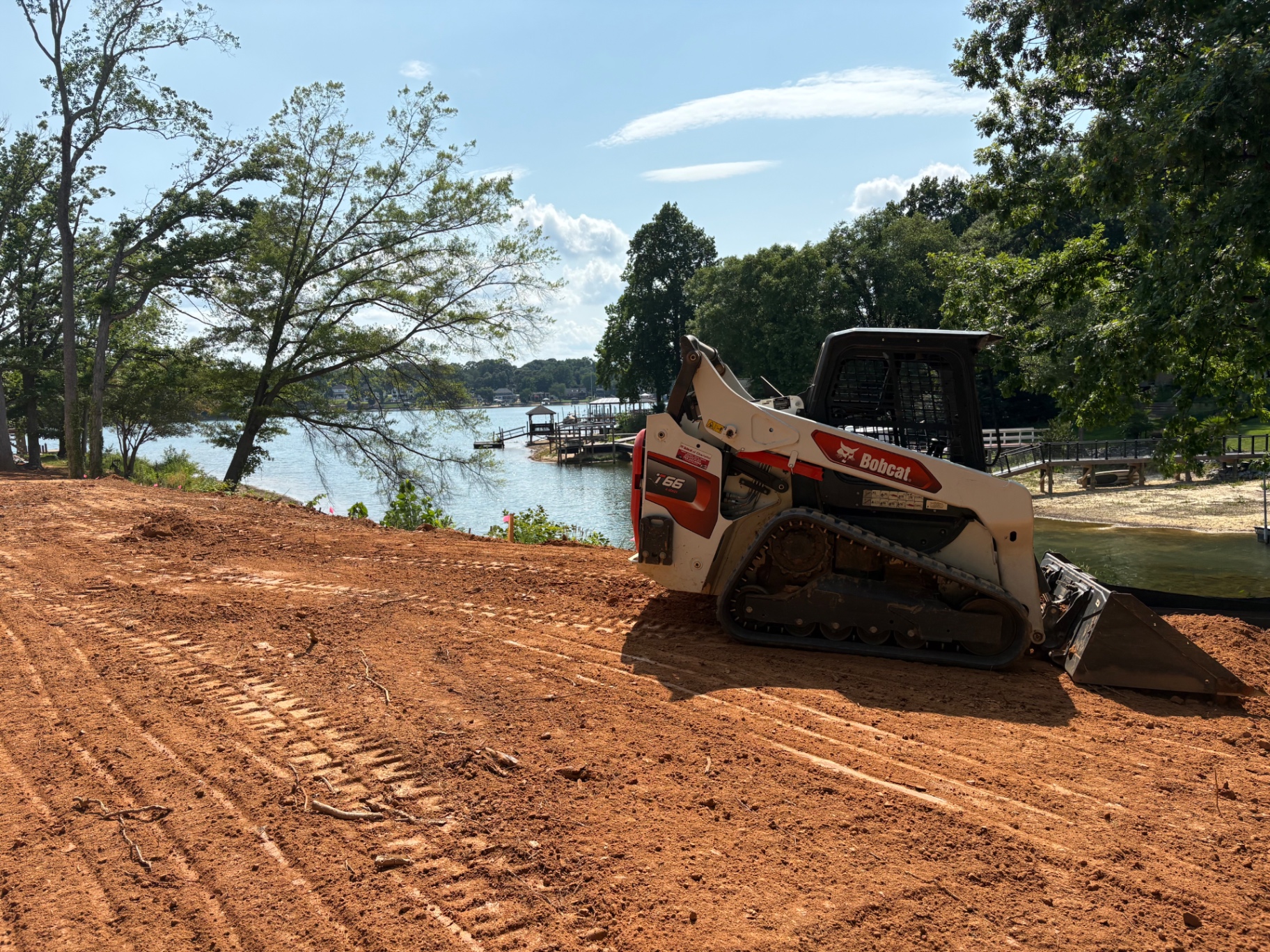 Compact track loader rough-grading red clay on a Lake Norman waterfront lot with silt fence along the shoreline in Cornelius, NC