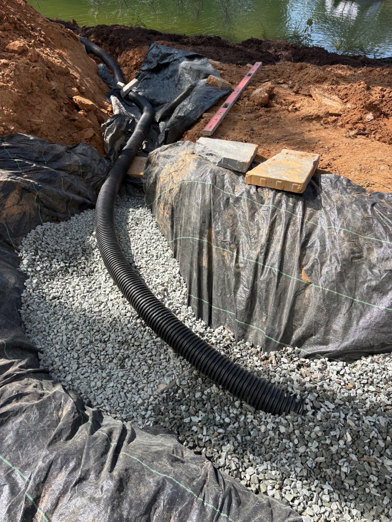 French drain perforated pipe bedded in washed gravel and filter fabric routed toward a pond in the Lake Norman area