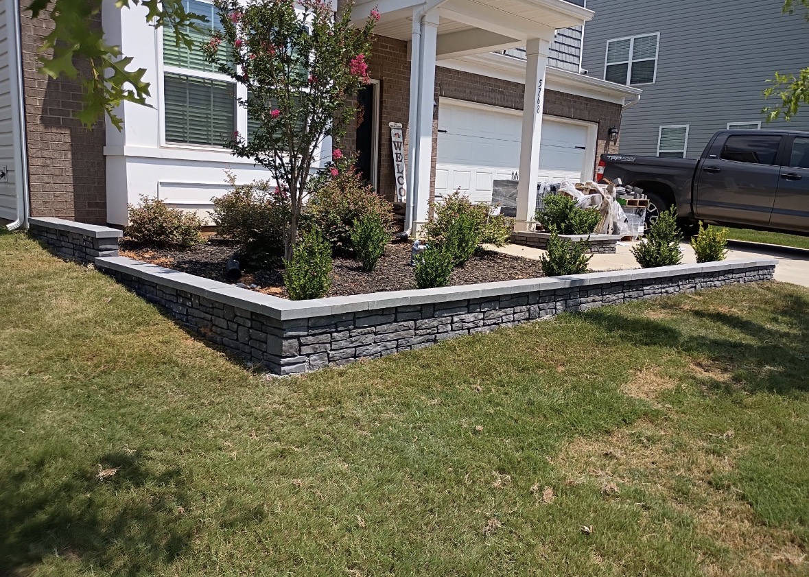 Charcoal stacked-stone seating wall with light gray caps framing a front planting bed in Mooresville, NC