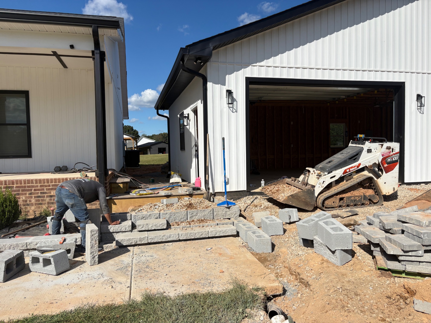 Crew building a block retaining wall and steps with a compact track loader beside a home