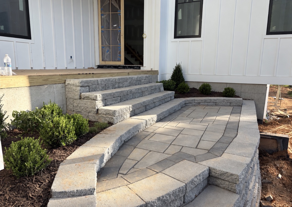 Light gray paver entry landing with wide block steps, curved seating walls and new foundation plantings at a Lake Norman area home